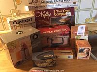 Photo showing boxed Cuisinart salt and pepper mills, Hometrends Single Serve Blender, The Nifty 3-Tier Oven, Apple Peeler, Aerolatte frother, magnetic utensil holder, and more boxed kitchen items.