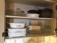 Shelves with white CorningWare casserole dishes with blue cornflower pattern, clear glass bowls and bakeware items