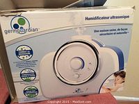 Photo of sealed original box of GermGuardian Ultrasonic Humidifier Model H2000 showing product image, branding, and features in French.