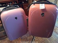 Pair of pink Heyes hard-shell carry-on luggage standing side by side on wood floor in room with furniture.