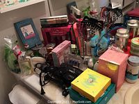 Photo showing multiple ladies personal care items including hair irons, boxed soaps, a mirror, gift packs, and hair accessories on a white surface.