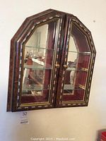 Front view of the wooden framed hanging knick knack shelf unit with glass doors and mirrored back reflecting shelves inside.