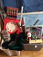 Two bins filled with assorted Christmas items including wrapping paper rolls, holiday crackers, stockings, ornaments, and decorative plates.