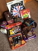 Photo showing a collection of games including a dartboard, a box of Apples to Apples game, Scrabble game, a chess set, and various other boxed games and puzzles.