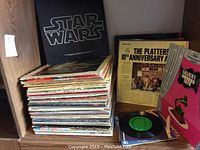 Stack of vinyl record albums including Star Wars soundtrack, The Platters 10th Anniversary, and a Grammy Winners album, arranged on a wooden shelf.