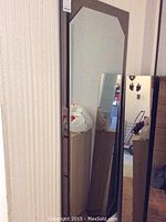 One larger decorative wall mirror with beveled edges leaning against wall.