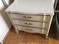Front angle view of the small vintage style dresser with three curved drawers and decorative metal handles, cream finish.