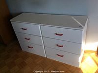Front view of white dresser with six drawers and red handles, showing surface and corner wear.
