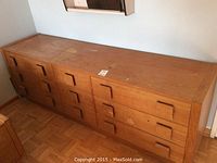 Full view of teak dresser showing eight drawers with square handles, finish with wear and marks on top surface.