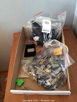 Photo of cardboard box containing plastic bags full of small locks and keys, a green army knife, and metal nail clippers.