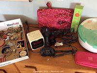 Photo of personal care items arranged on wooden surface including jewelry, clock radio, hair dryer, flat iron, cosmetic bags and HoMedics foot spa.