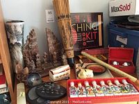 Overview of oriental items including Thai umbrella, wooden sculptures, iron balls, small decorative bottles, Chinese character box, cat figurine, and an I Ching Kit book.