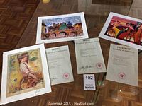 Three seriolithograph prints laid out on a table with their respective certificates of authenticity from Park West Galleries.