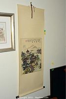 Full view of the scroll painting hanging on a white wall with framed artwork beside it.
