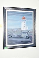 Full view of the framed oil painting showing the lighthouse on rocky shore under a blue-gray sky.
