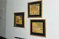 Three framed Asian style watercolour paintings hung on a white wall in a cluster, each with gold bamboo-style frames and black mats.