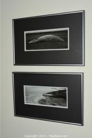 Two black and white framed photographic prints hanging on wall, featuring an overturned boat and a shoreline scene.