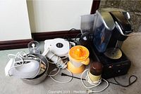 Keurig coffee maker, waffle iron, citrus juicer, Salton scale mixer and other appliances grouped together on floor