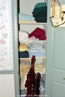 Shelving unit with folded towels and linens in various colors and a burgundy upright vacuum cleaner.