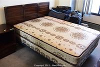 Double bed with mattress and box spring on a metal frame, with wooden headboard, showing stains and wear on mattress and box spring