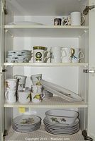 Four shelves of Noritake dinnerware and mugs including plates, bowls, cups, and serving pieces, showing overall lot contents.
