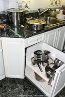 Countertop: large stockpot with lid, sauté pan, stainless funnel and manual citrus juicer next to sink