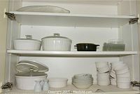 Glass-front cabinet shelf with 4 Corningware casseroles and glass dishes on top shelf, custard cups and plates on lower shelf