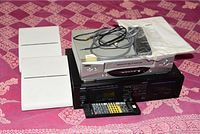 Silver Grapevine VCR with cables and manual on top, placed on Yamaha cassette deck, with remote control in front and white speakers on the side.
