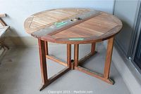 Full view of the round wooden patio table with drop leaf extended, showing legs and frame.