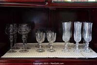 Full view of three different styles of crystal stemware including large etched bowls, smaller diamond cut wine glasses, and tall champagne flutes with vertical cuts.