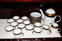 Full display of Fitz and Floyd tea set pieces including cups, saucers, cream, sugar, and teapot all arranged on cloth.
