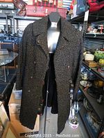 Front view of the black Persian lamb fur coat on a mannequin, showing the double breasted buttons and the notched collar.