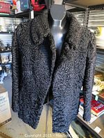 Front view of black Persian lamb wool jacket on mannequin showing notched collar and curly textured fur.