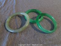 Three jade bangle bracelets displayed on grey fabric