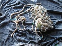 Overall view of the three pearl necklaces laid out on dark fabric showing varying sizes and shapes, some green beads included.