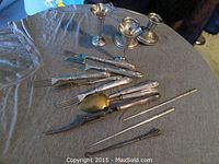 Photo showing two bud vases, two taper candle holders, and assorted cutlery including forks, spoons, and a knife, all in sterling silver with a bit of tarnish
