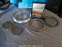 The four round silver trivets and the wine bottle holder arranged on a cloth surface.