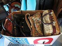 Top view of box containing six purses with different materials including leather, beaded, floral tapestry, and wicker.
