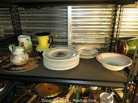 Shelf with stacked plates, ceramic jugs, and large bowl showing variety in the lot.