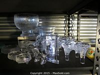 Full assortment of clear glass pieces on shelf, showing bowl, vases, dishes, candle holders, tripod bowls, block and figurine