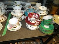Collection of 18 assorted china cups and saucers on a table, featuring various floral patterns and colors.