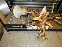 Chandelier parts on black shelving including glass light shade, gold metal frame with leaf designs, and boxes of crystal prisms.