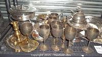 Multiple silver plated goblets, trays, cutlery, and other items arranged on a shelf to show condition and variety of the lot.