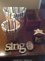 Overall lot showing two woven baskets with fabric liners, stone word figurine 'sing', rectangular storage container, and cylindrical decorative box labeled 'friends'