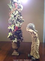 Full view of artificial vine topiary in ornate artificial stone planter next to hide and seek child figurine