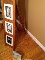 Wooden floor standing picture frame leaning against wall with three vertical slots showing black and white photos inside.