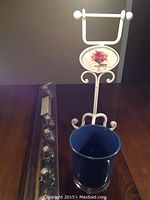 Wrought iron toilet paper holder with blue ceramic waste bin and unopened plastic package containing shower curtain hooks and rod.