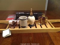 Full view of all items on rubberwood tub tray showing soap dispenser, stone cup, bath oil bottle with dried flowers, French milled soap, flat iron in box, terry bath pillow and tray