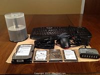 Computer peripherals including keyboard, mouse, USB hub, blank DVD spindle, and multiple hard drives arranged on a table.