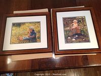 Two framed prints with wooden veneer frames placed side by side on a wooden surface, showing children in nature scenes.